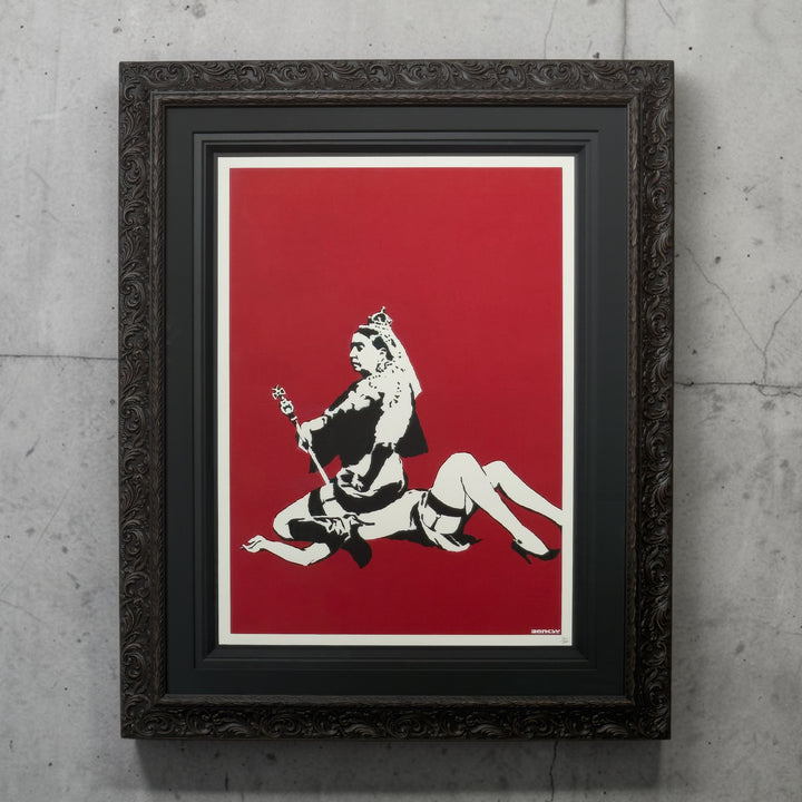 Framed Banksy artwork - Queen Vic with a black and white screen printed art on a red background, displayed on a textured grey wall.