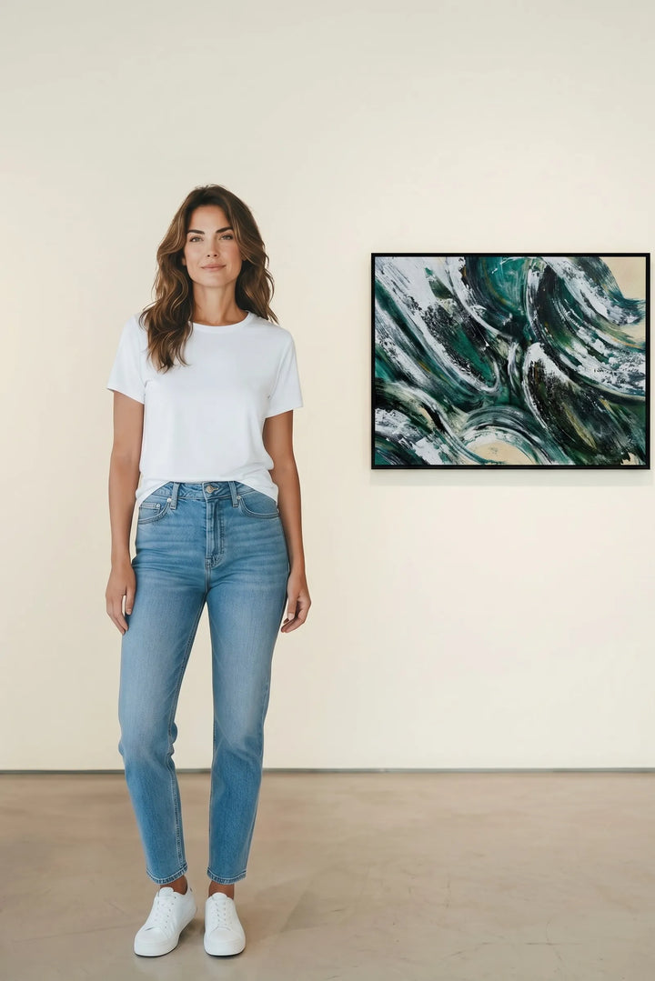 Woman wearing a white t-shirt and blue jeans standing in front of abstract wall art by Charlotte Gibbs.