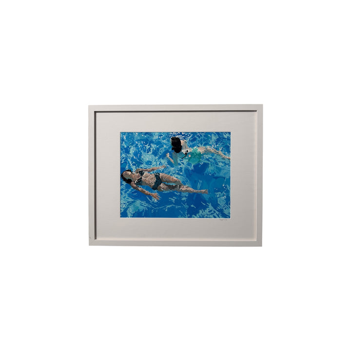 A framed art print featuring an overhead photograph of two people swimming in a bright blue pool, set in a light gray frame against a white background.