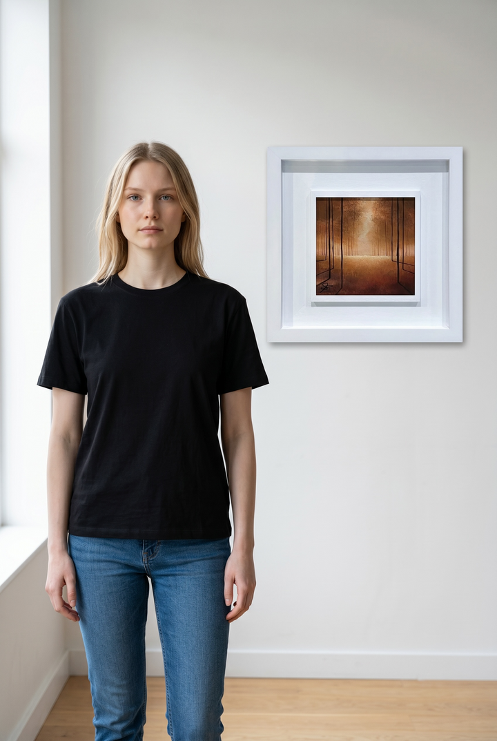 Person wearing a black t-shirt and blue jeans standing in a room with a framed artwork by Vincent Devine on the wall.
