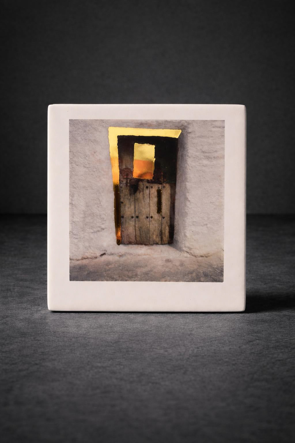 Framed photograph on porcelain of a door with light coming through on a dark background