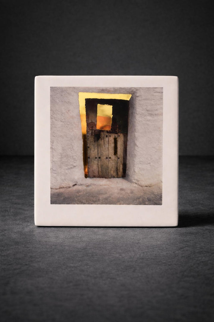 Framed photograph on porcelain of a door with light coming through on a dark background