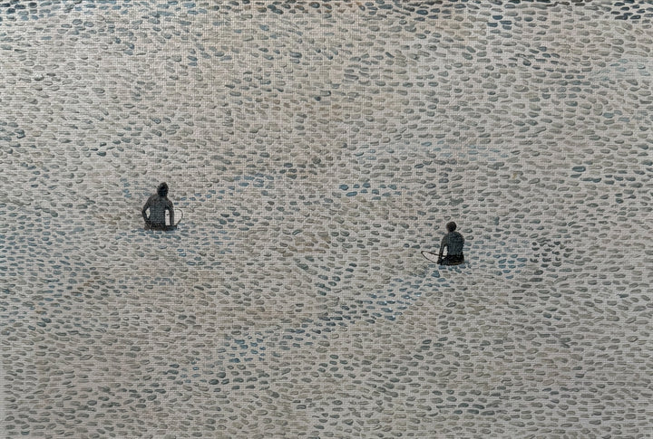 Two surfers sitting on a textured water surface waiting for a wave