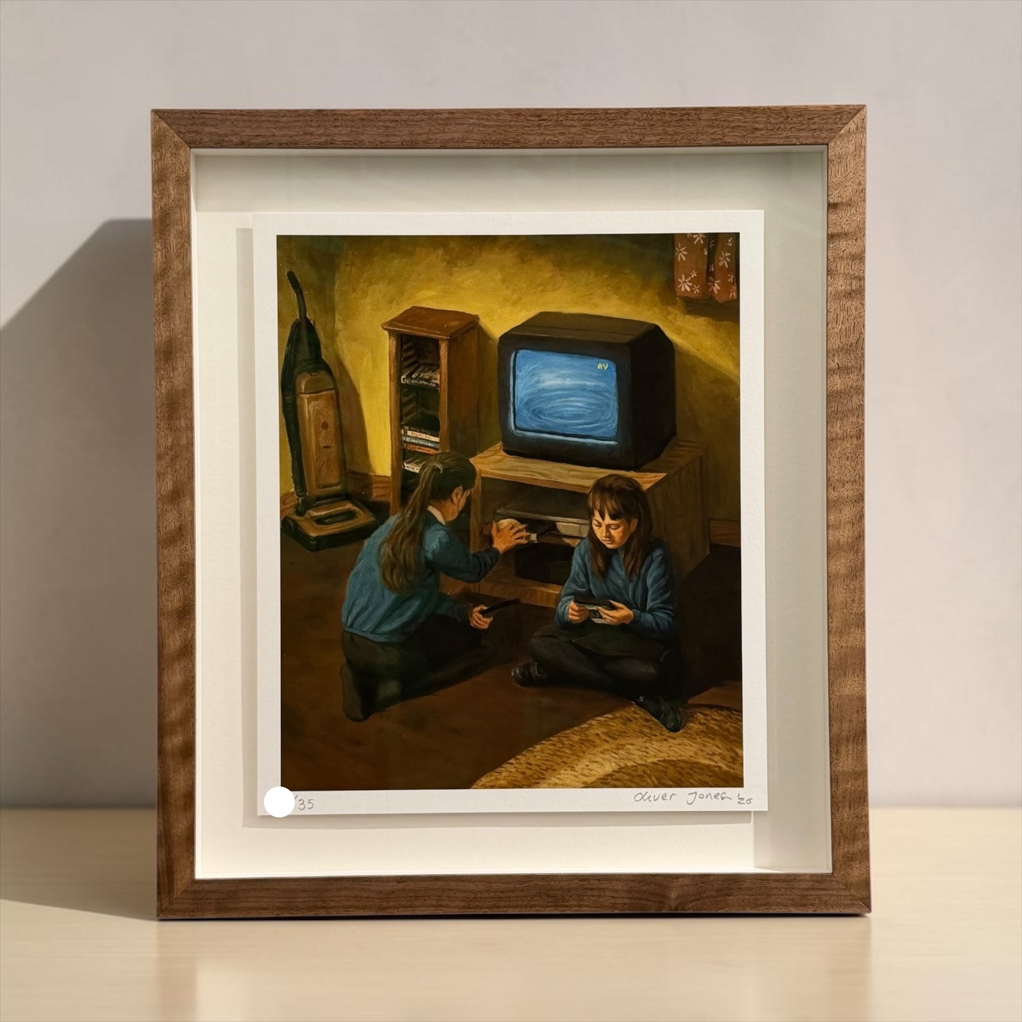 A framed art print depicting two children in a dimly lit room with a vintage television set, mounted on a light-colored wall above a white surface.