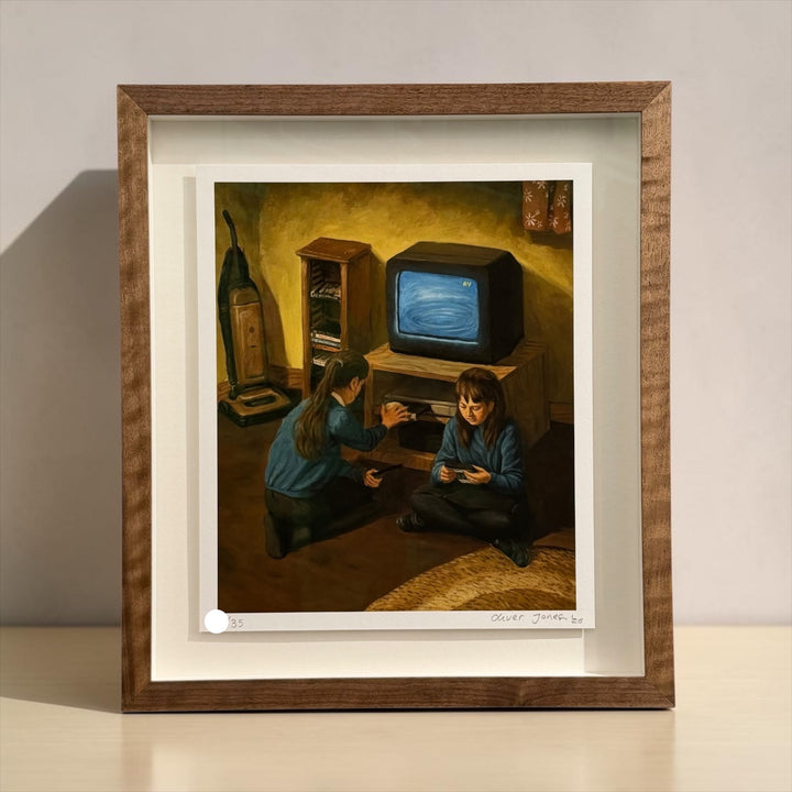 A framed art print depicting two children in a dimly lit room with a vintage television set, mounted on a light-colored wall above a white surface.