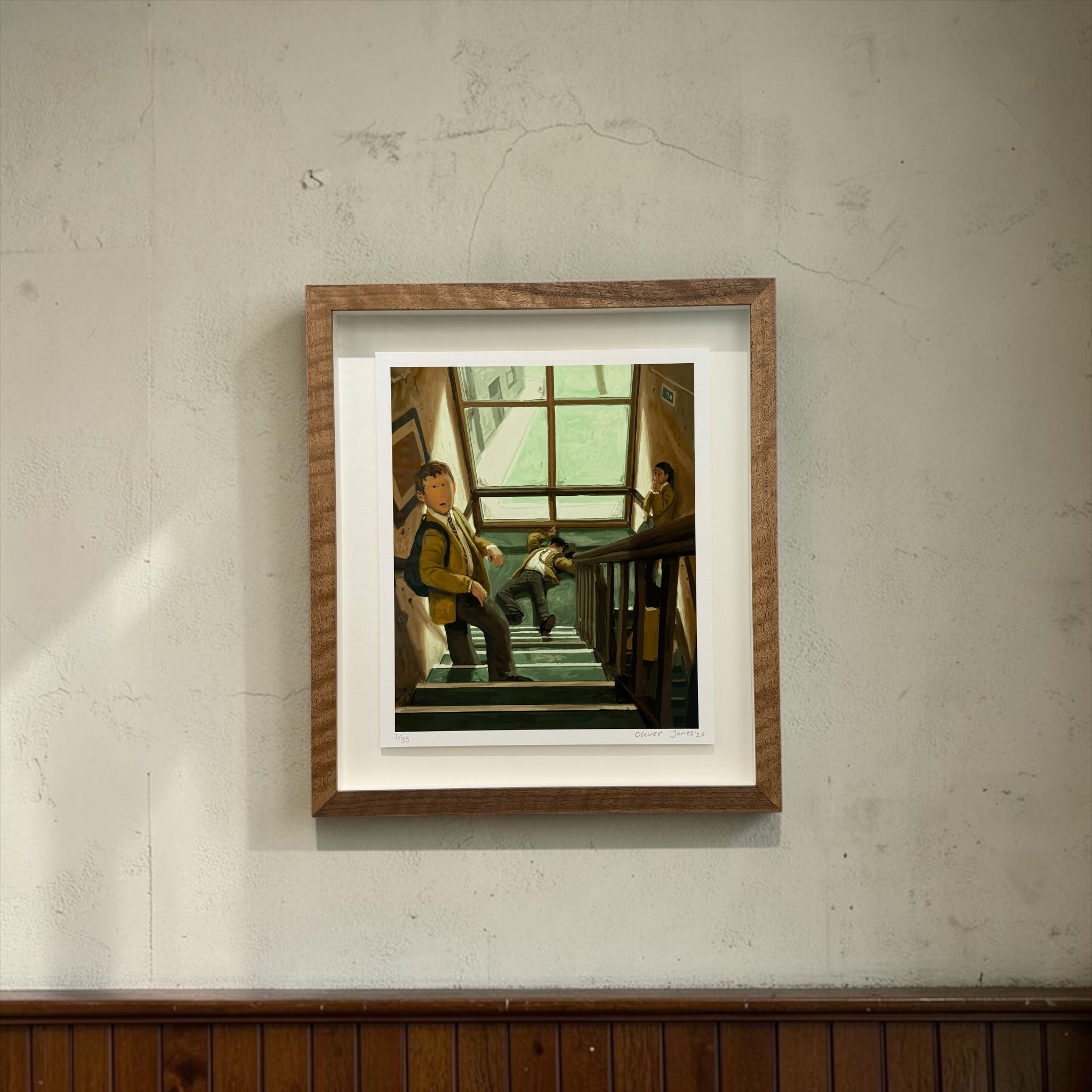 A framed art print depicting a scene of people on a staircase, mounted on a textured light gray wall above a dark wood panel.