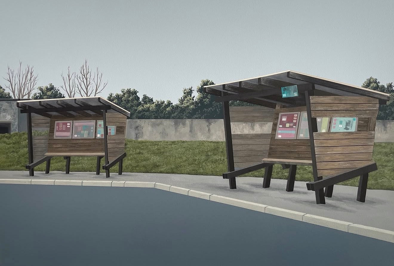 Two modern wooden bus stop shelters with integrated benches, set on a paved area next to a body of water, with a grassy field and trees in the background.