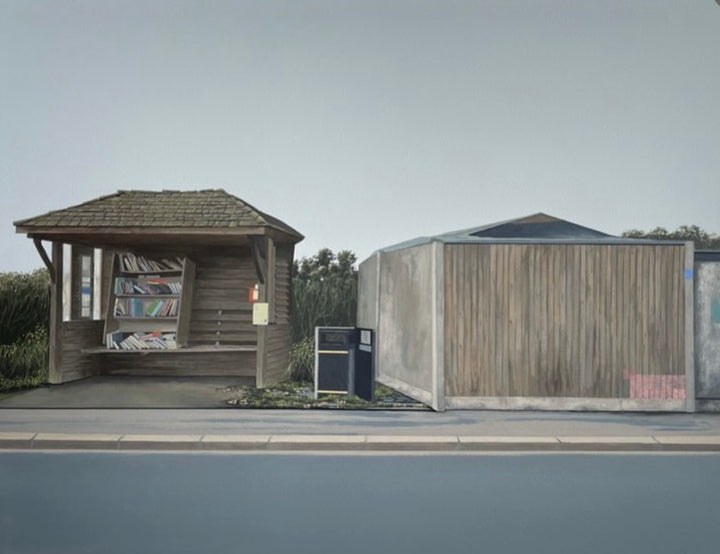 A wide outdoor scene showing a small wooden shelter with a bench and bookshelves beside a larger wooden structure, set near a road under a pale sky.