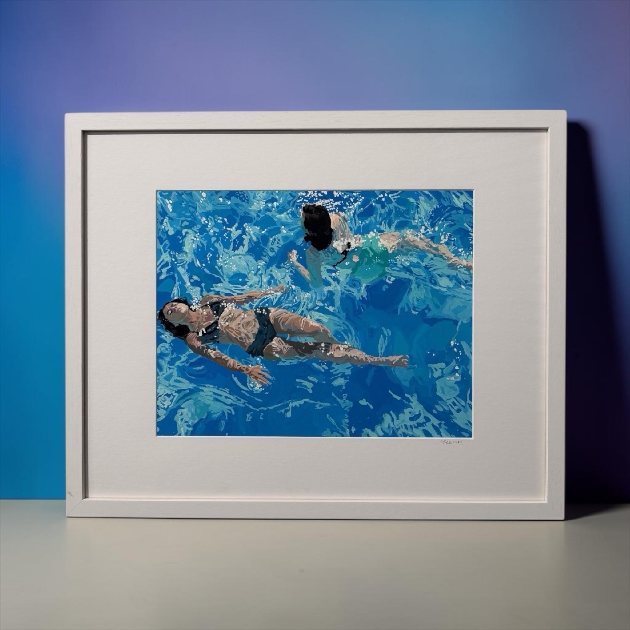 A framed art print depicting two women swimming in a bright blue pool, presented in a white frame against a blue gradient background.