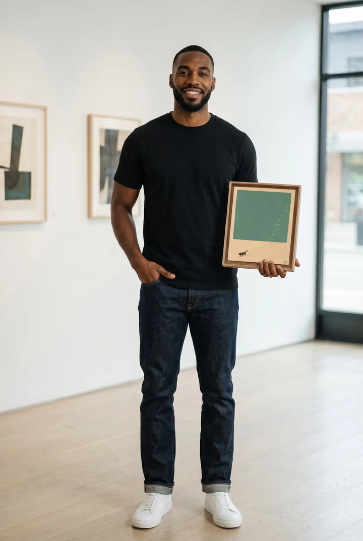 Man holding a framed artwork by laine jones in a room with light-colored walls and wooden floors.