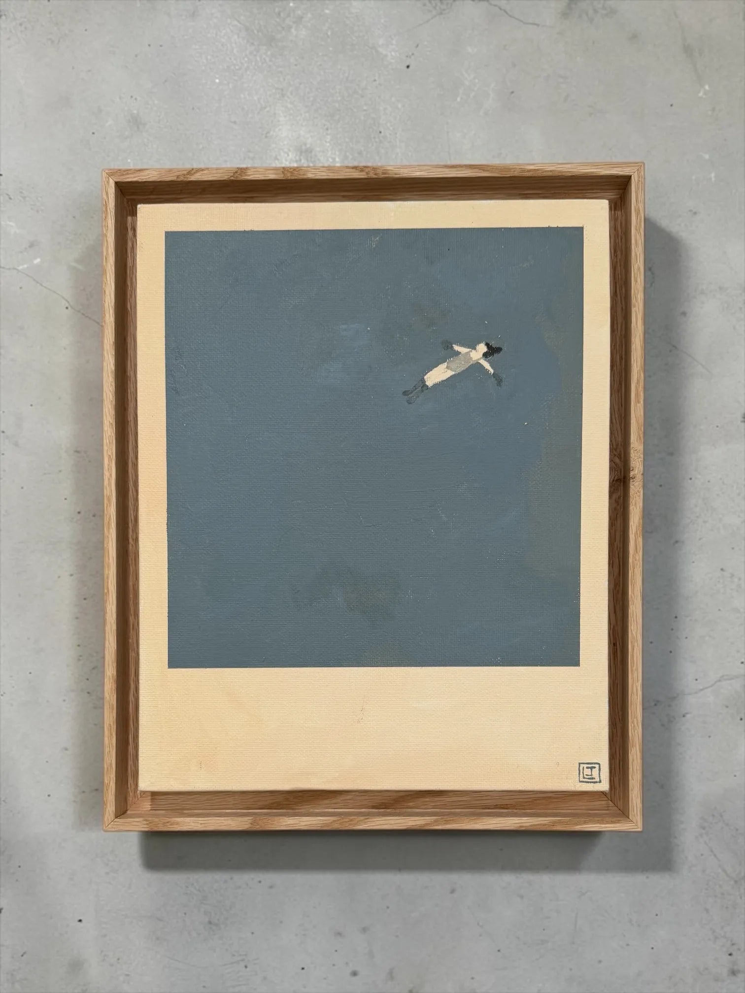 Framed Laine Jones 'Drift" artwork of a small figure drifting on a blue sea, mounted on a concrete wall.