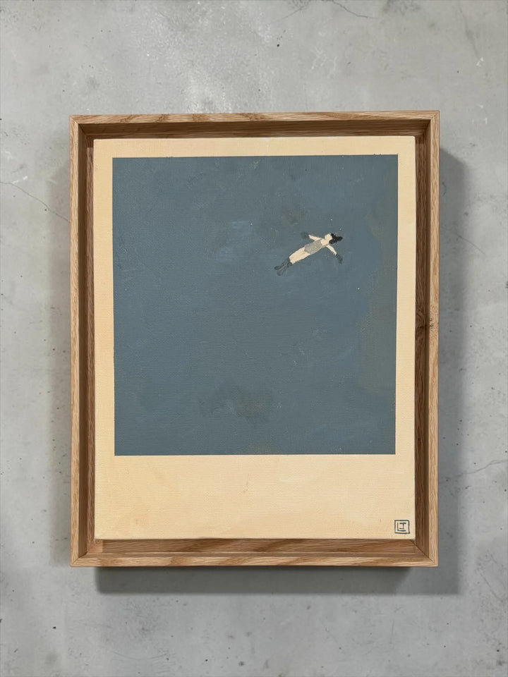 Framed Laine Jones 'Drift" artwork of a small figure drifting on a blue sea, mounted on a concrete wall.
