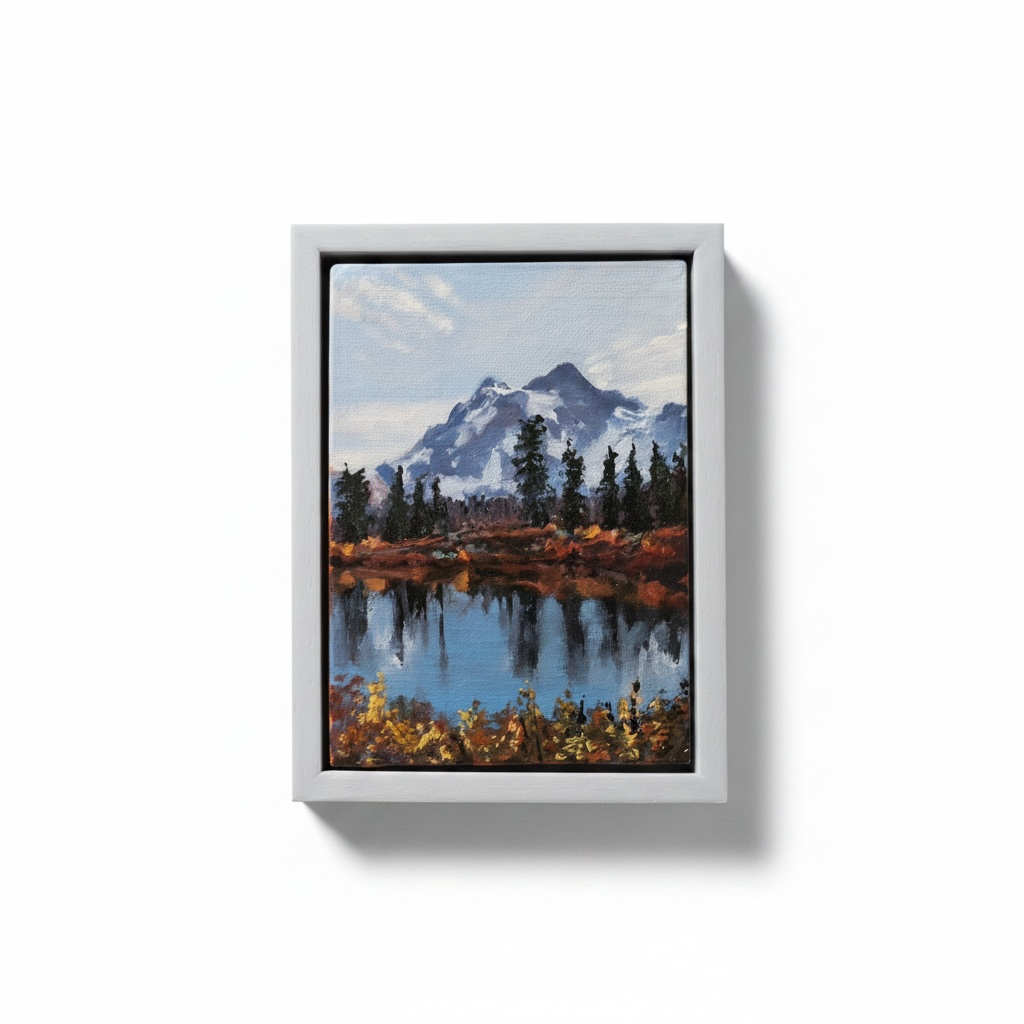 Framed painting of a mountain landscape with a lake on a white wall.