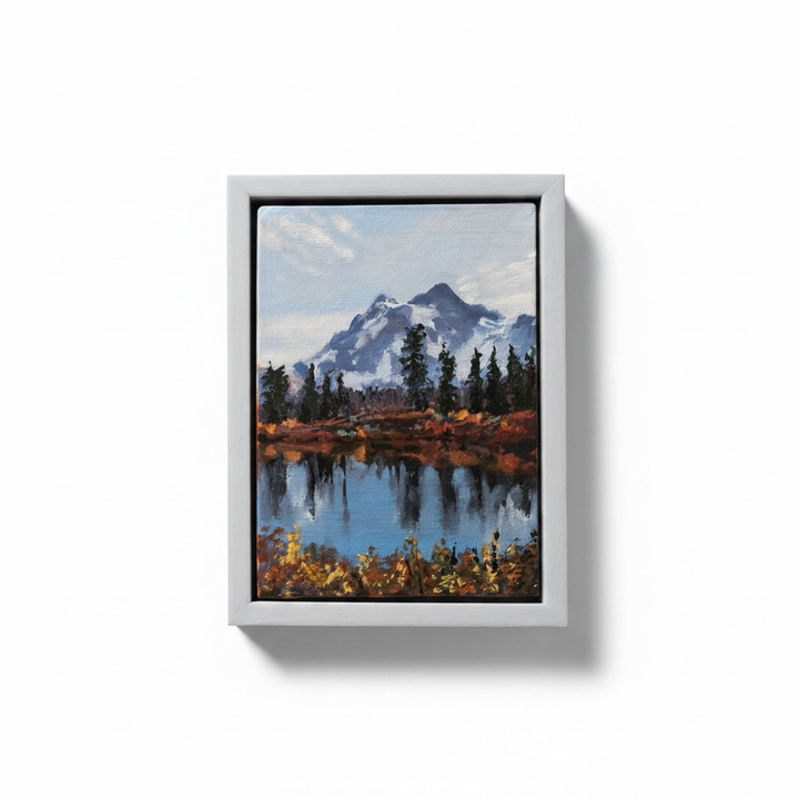 Framed painting of a mountain landscape with a lake on a white wall.